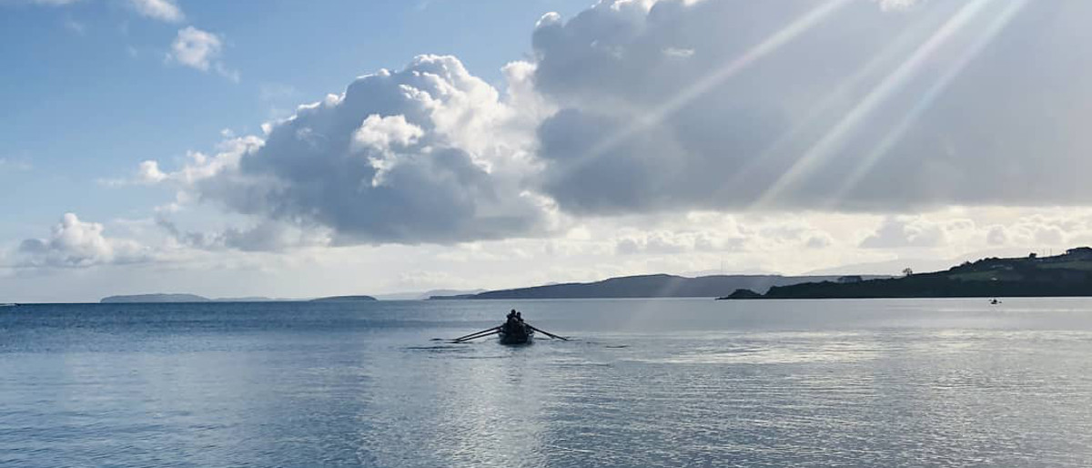 A coastal rowing boat heading towards Ynys Môn